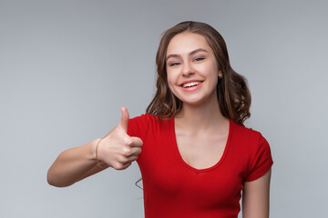 Image of happy young brunette woman isolated over gray background showing thumb up gesture