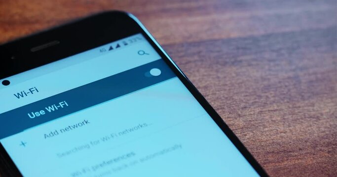 Person chooses wi-fi and enters password to engage with contemporary smartphone by finger on wooden table extreme close view