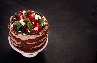 Delicious homemade chocolate cake with fresh berries and mascarpone cream on dark background.