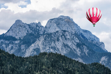 A great view of the high Alps mountains wth green forest and a hot air balloon under blue cloudy sky.