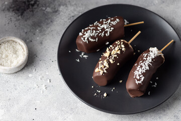 Frozen bananas in dark chocolate with nuts and coconut on dark plate. Healthy vegan dessert concept. close-up