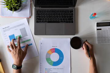 Top view of male hands holding a cup of coffee working on laptop calculator financial report and medical face mask on desk, business accounting with new normal during Covid 19 pandemic concept