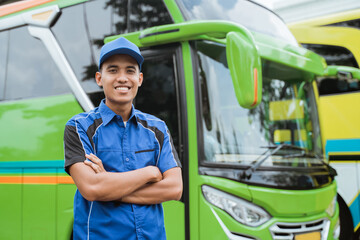 A handsome bus driver in uniform and hat smiles crossed hands with the background of the bus