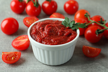 Bowl of tomato paste and tomatoes on gray textured background