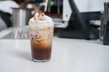 Iced mocha cola latte. A glass of coffee mixed with cocoa syrup and cola drink, topped with whipped cream on white table.