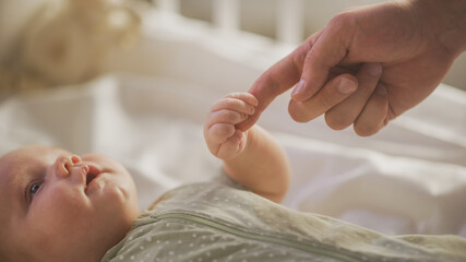 Close Up Shot of Newborn Baby Playing With Mother's Hand and Finger while Lying on the Back in Child Crib. Caucasian Neonate Toddler Bodning with Mom. Concept of Childhood, New Llife and Parenthood