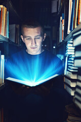 guy in the library. open book with fantastic light. the power of knowledge and reading books