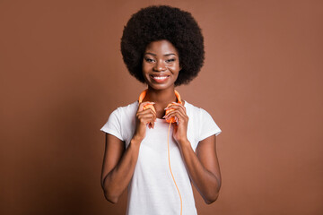 Photo of adorable dark skin lady hands touch headphones hang on neck toothy smile isolated on brown color background