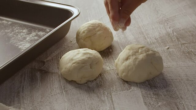 Male hands sprinkle a piece of baking dough with flour. Dough is lying on wooden table. Filmed on black background.