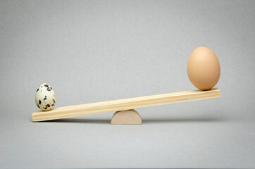 Selection and comparison of quail eggs or chicken eggs.  Wooden scales on a gray background. Balanced dietary nutrition.
