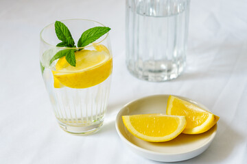 Ein Trinkglas mit Wasser, Zitrone und Pfefferminze auf einem weißen Tischtuch. Erfrischung, Diät, Sommer.
