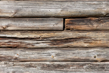 Obraz premium The wall of an old wooden house built from round pine logs. The logs are rotten and crumbling. A hole is visible in the wall.