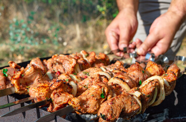 Man prepare juicy slices of meat with sauce on open fire. Grilling a barbecue outdoors.