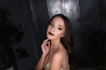 Fototapeta na wymiar Close up beauty portrait of a brunette girl with brown eyes, professional evening make-up, dark lipstick, smoky eyes in a gold corset. A festive image for a party. Silver dark background. Copy space