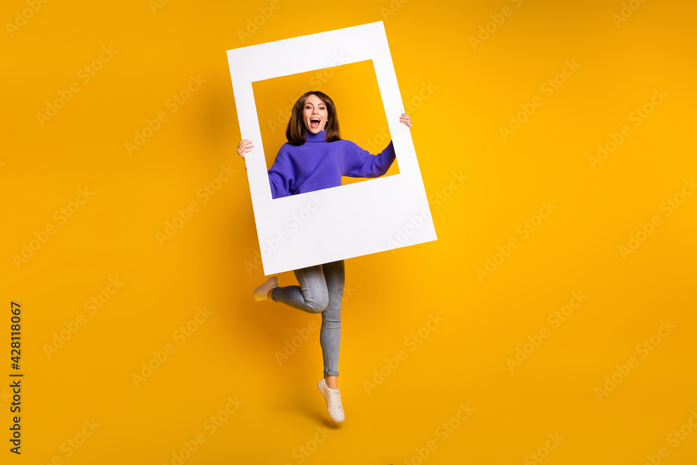 Sticker Full length body size view of attractive cheerful girl jumping holding big paper frame having fun isolated over bright yellow color background