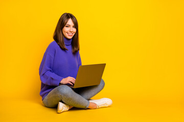 Full size photo of young smiling good mood girl sit on floor working in laptop isolated on yellow color background