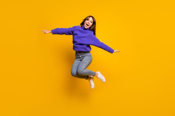 Fototapeta na wymiar Photo of funny pretty young woman wear purple pullover jumping high arms hands sides isolated yellow color background