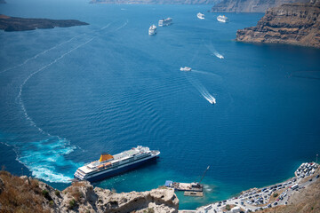 A ferry arriving to the port of Santorini on a hot summer day, boats in the caldera.