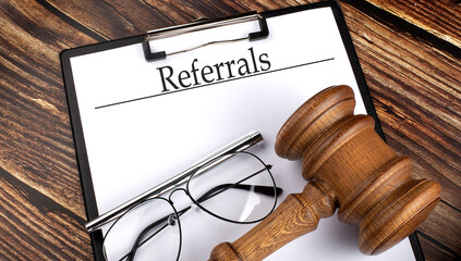 REFERRALS with gavel, pen and glasses on the wooden background