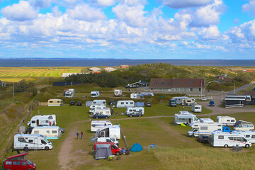 Fototapeta na wymiar View over camper vans and caravans at camping site among dunes to the Ringkobing fjord at horizon (Hvide Sande, Denmark)