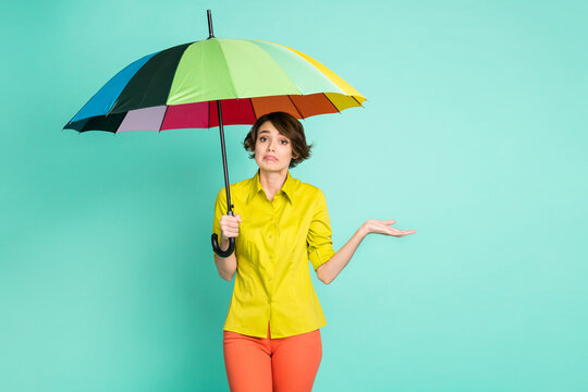 Photo portrait of sad grumpy woman keeping umbrella in rainy weather isolated on vibrant turquoise color background