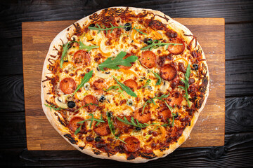 Appetizing fresh hot pizza with salami and oregano on an oak board against a dark wood table background