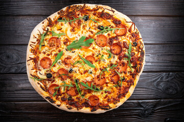 Bright appetizing fresh hot pizza with salami, olives, mushrooms and oregano on a dark textured wood table background