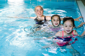 Mother with two daughters having fun in indoor swimming-pool. Girl is resting at the water park. Swimming school for small children. Concept friendly family sport summer vacation. Selective focus