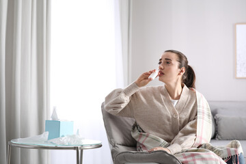Sick young woman using nasal spray at home