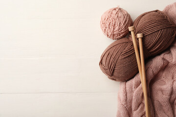 Woolen yarns, knitting needles and sweater on white wooden background, flat lay. Space for text