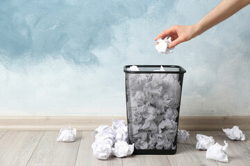 Woman throwing crumpled paper ball into basket near light blue wall, closeup. Space for text