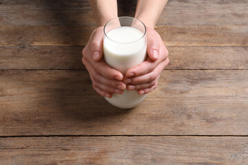 Woman holding glass of milk at wooden table, closeup