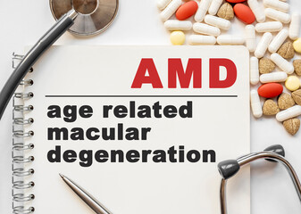 Page in notebook with AMD age related macular degeneration on white background with stethoscope and group of pill. Medical concept. Term and abbreviation