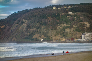 San Sebastian, Spain - March 15, 2021: Surfers on Zurriola Beach on a winter day in San Sebastian