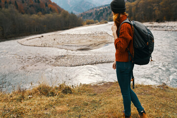 woman travel in the mountains on nature in autumn near the river and backpack hat sweater vacation