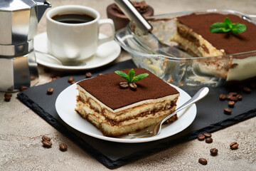 Traditional Italian Tiramisu dessert in glass baking dish and portion on grey concrete background