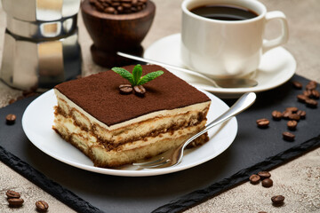 Portion of Traditional Italian Tiramisu dessert and mocha coffee maker on grey concrete background