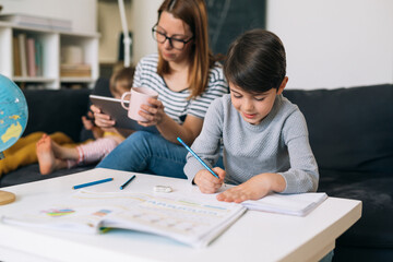 little boy does his homework at home. mother sitting beside him