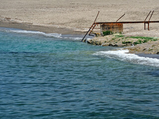 Broken, metal, rusty staircases with damaged railings lead to the sea. Waves run over the rocky...