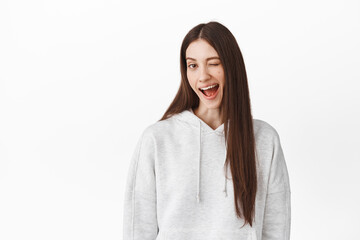 Fototapeta premium You got this. Positive cheeky girl winking and smiling, hinting on something, encourage you, praise excellent choice, make sly hints, standing against white background