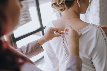 gathering of the bride, buttoning up a wedding dress close-up, buttons and woman's hands, an...