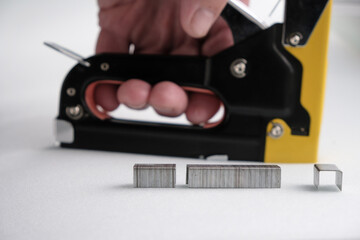 Metal staples on a blurred background of a staple gun in a man's hand. White foam rubber background. 