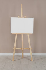Wooden easel with blank canvas near beige wall