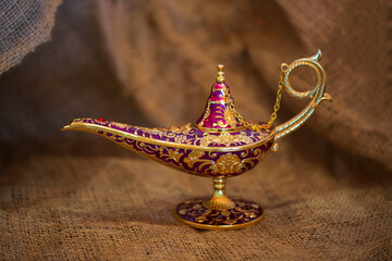 Golden magic genie lamp on burlap background, close up. lamp of desires from the story of Aladdin...