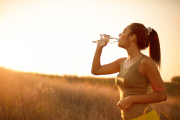 Time for refreshing.  Sporty young woman drinking water outdoors.