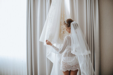 morning of the bride, getting ready, the bride in a robe holds a wedding dress hanging on a hanger