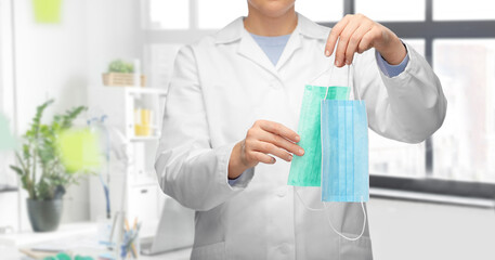 medicine, health protection and healthcare concept - close up of female doctor in white coat showing two masks over medical office at hospital on background