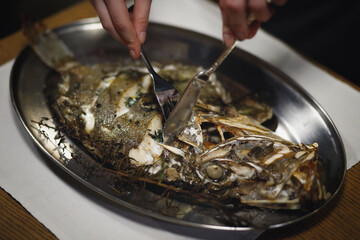 The girl cuts with a knife and fork a fresh fried dorado. Sea fish on a silver plate.