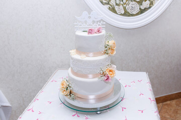 A large white wedding cake with figures of birds on a wooden stand in a restaurant. Cake for the bridal wedding ceremony.