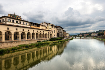 Fototapeta na wymiar Florence. Arno River view from the Medieval Ponte Vecchio (Old Bridge). On the left the Vasari Corridor (Corridoio Vasariano, 1565), which connects Palazzo Vecchio with Palazzo Pitti. Tuscany Italy.